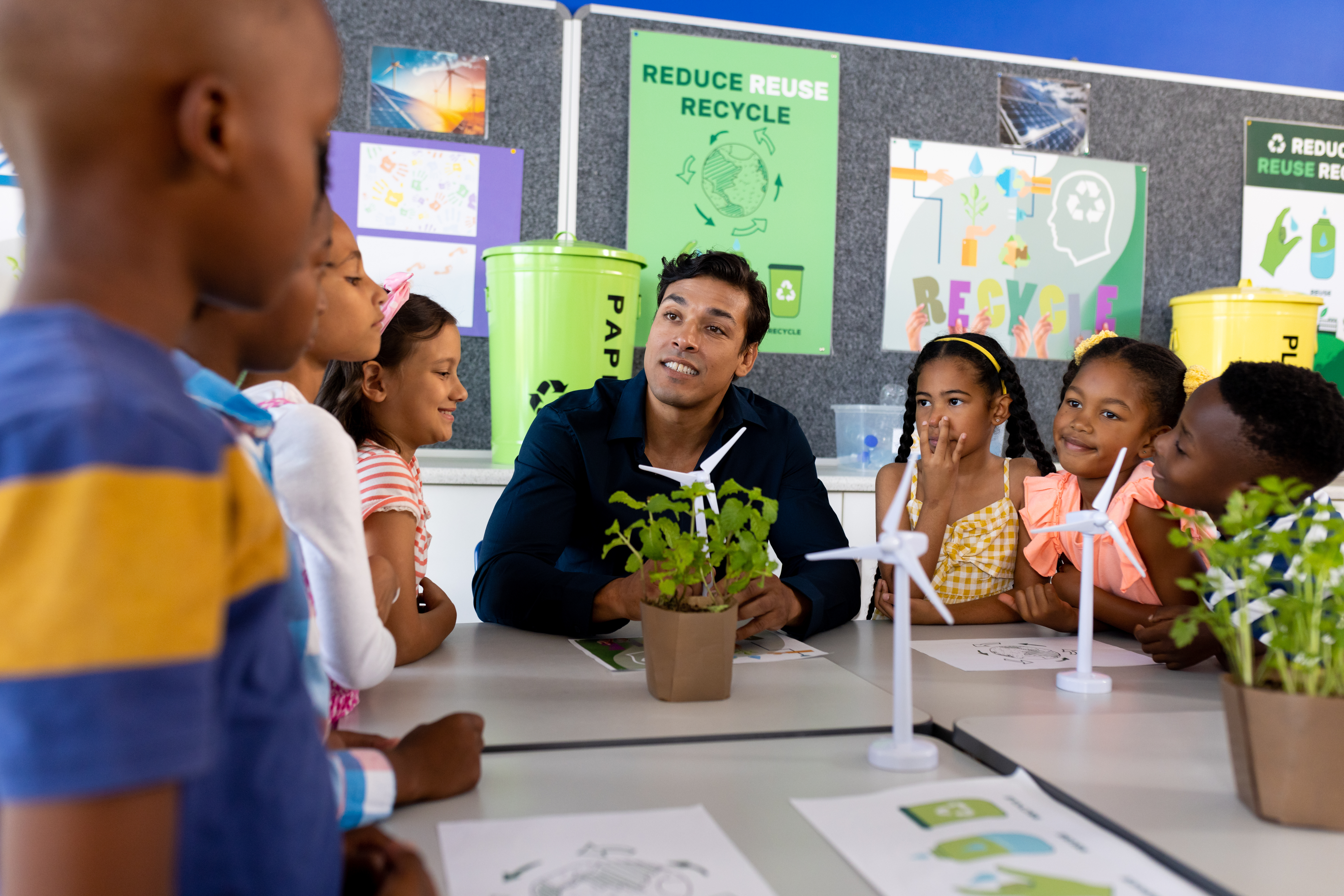 Teacher and children in classroom with miniature wind turbines and plants.